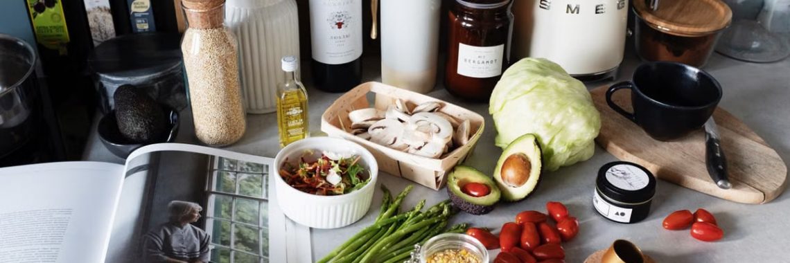 Various colorful healthy food and vegetables locating on countertop next to many different utensils and white kettle during cooking in stylish kitchen