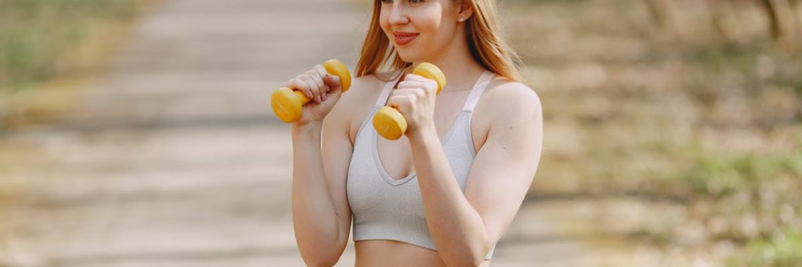 Fit woman lifting dumbbells on a sunny day, embracing a healthy outdoor workout.