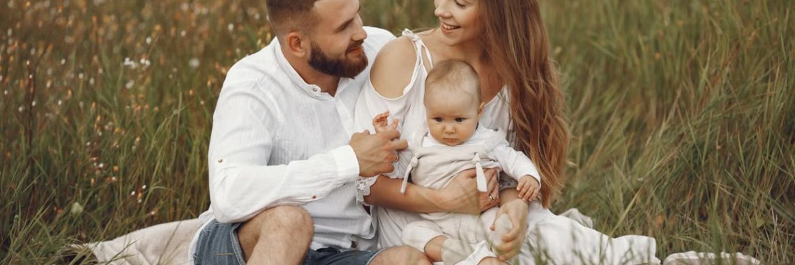 A joyful couple with their baby sitting on a blanket in a sunny meadow, embracing the beauty of summer.